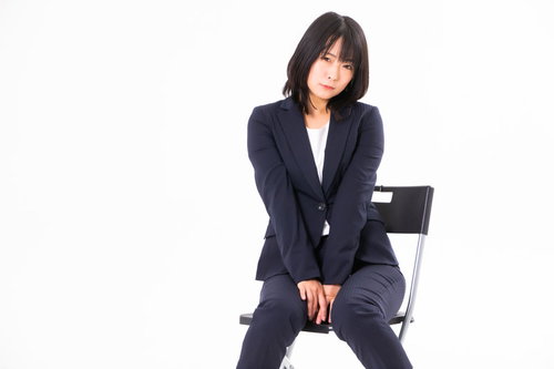 紺色のスーツを着てもじもじする女性社員が椅子に座る
