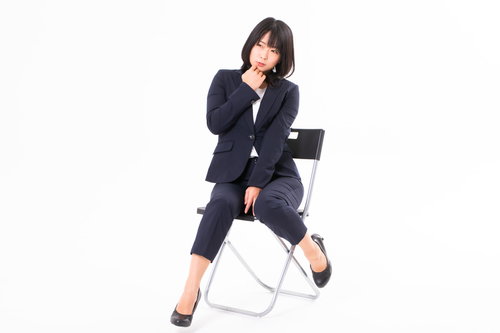 白い椅子に腰掛けてモジモジする女性社員のポーズ