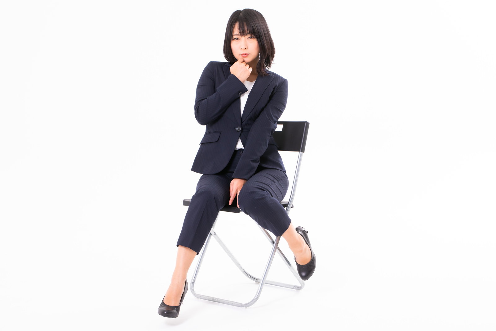 口元に手を寄せて思わせぶりな座り方をする黒いスーツの女性［モデル：にゃるる］