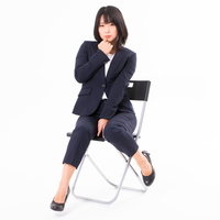 口元に手を寄せて思わせぶりな座り方をするOL女性の写真