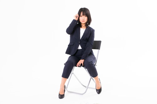 耳に髪をかけて考えるポーズの紺色スーツ姿の女性社員