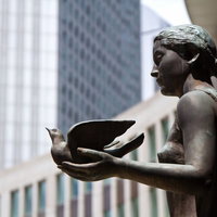 公園に立つ鳩を手に載せたブロンズ像の写真