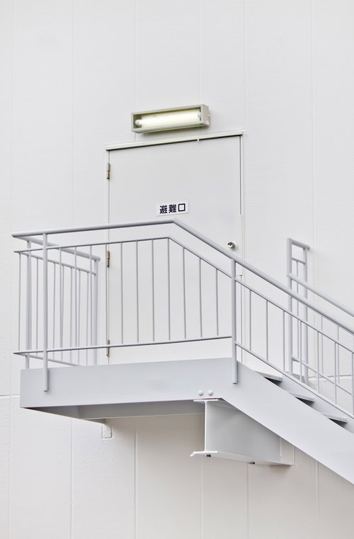 白い壁に緑の避難口サインがある非常階段