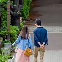 緑の並木道を手をつないで散歩する恋人の後ろ姿の写真