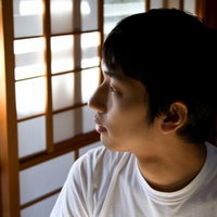 甚平姿で和室の縁側から外を見つめる男性の写真