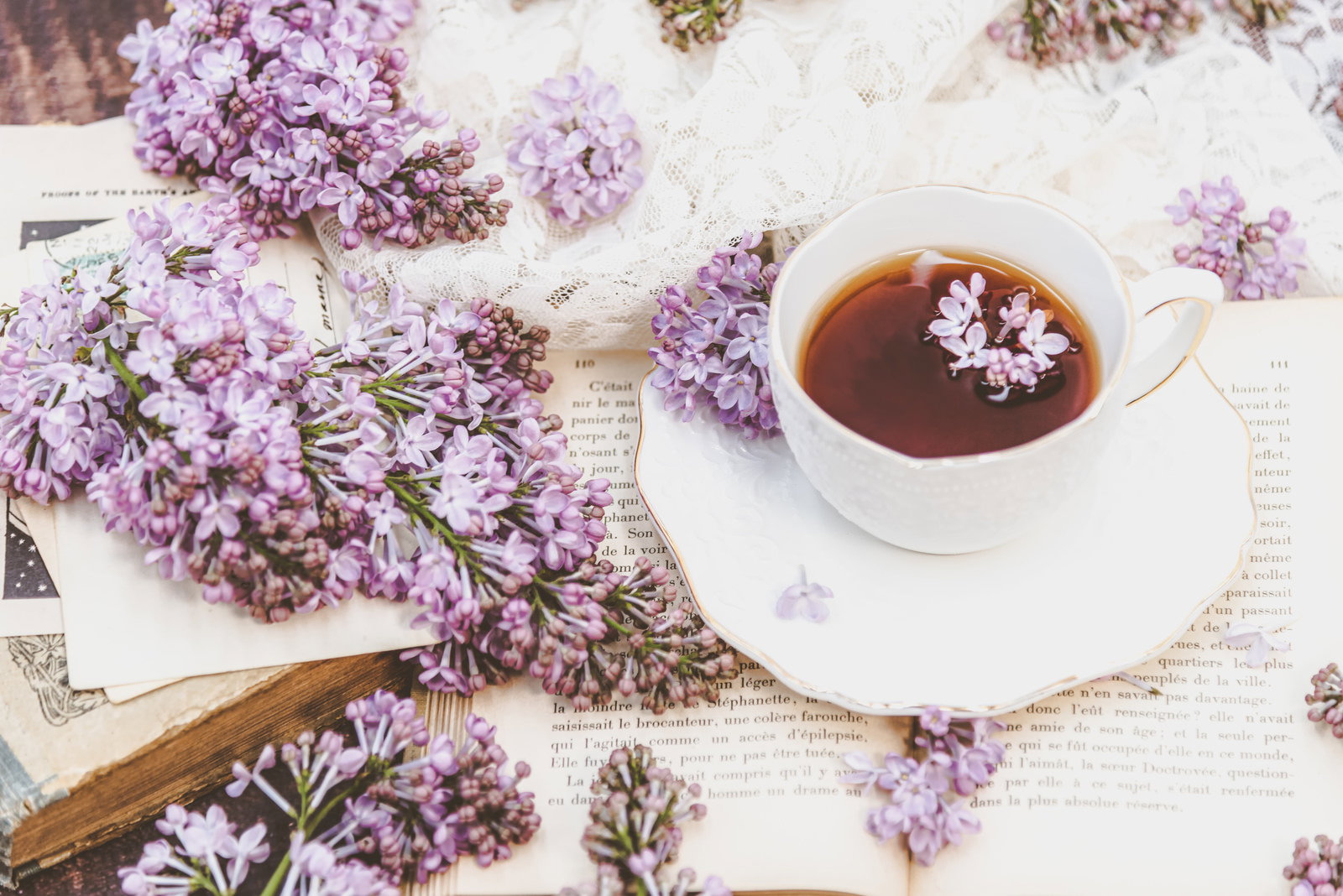 白いティーカップに入った紅茶と淡い紫色のライラックの花が散りばめられた優雅なティータイム