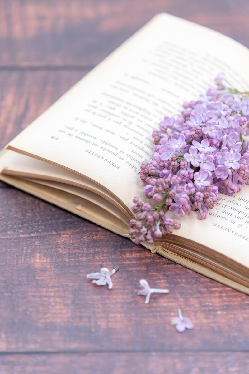 木製テーブルの上で開かれた洋書に紫色のライラックの花が挟まれている