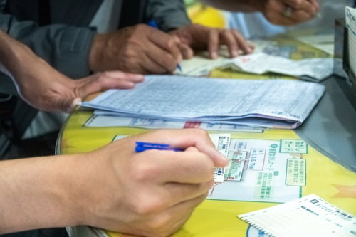 競馬場で馬券を購入する人たちの手元と競馬新聞への記入風景