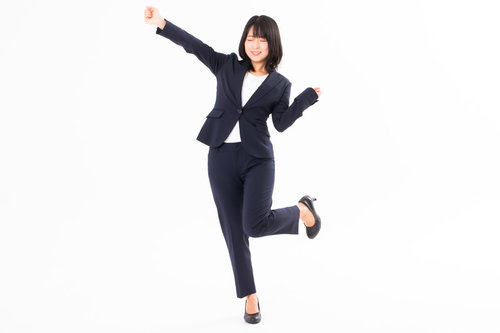 黒いスーツを着た女性社員が手を上げて喜びを表現するポーズ