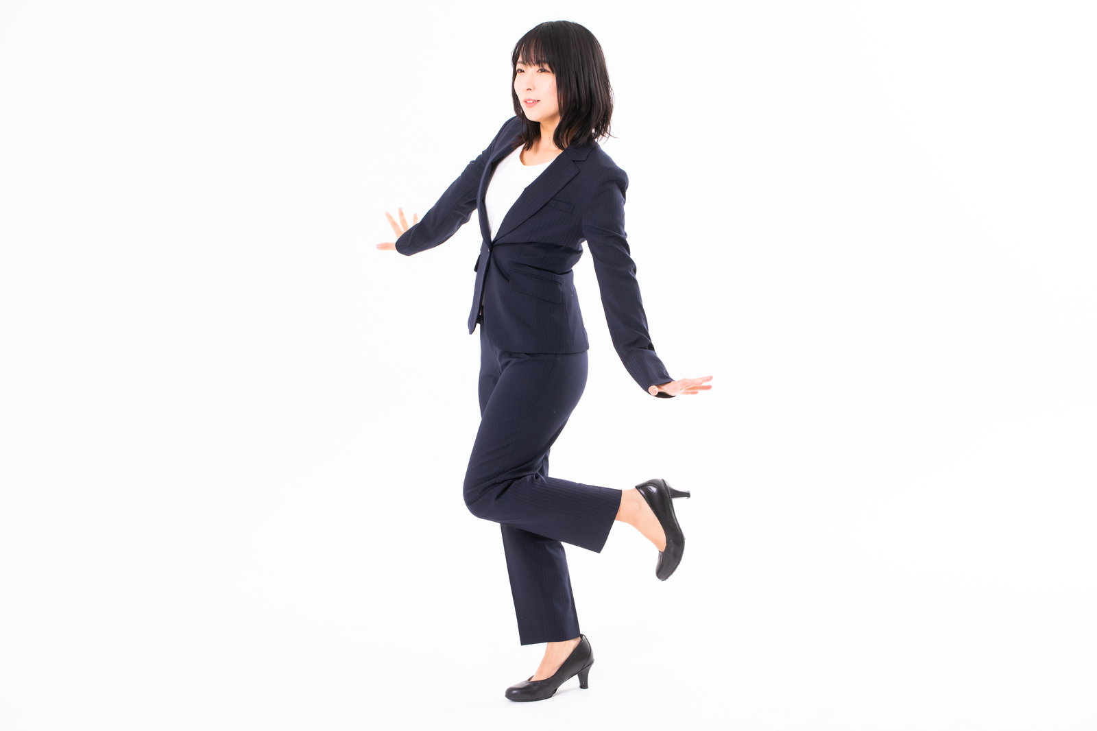 紺色のスーツを着て片足を上げ喜びのポーズを決める女性社員［モデル：にゃるる］