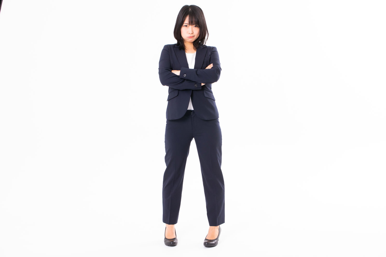 黒いスーツを着て腕組みをし、怒った表情を見せる女性社員［モデル：にゃるる］