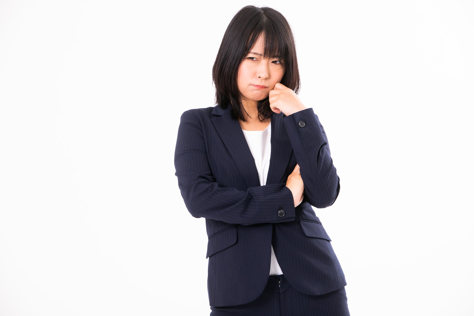 紺色のスーツを着て腕を組み、困惑した表情を見せる女性社員［モデル：にゃるる］