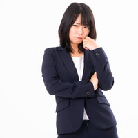 紺色のスーツを着て腕を組み悩む女性社員の困惑した表情の写真