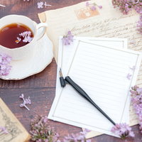 ティーカップに浮かぶライラックの花弁と白紙の手紙の写真