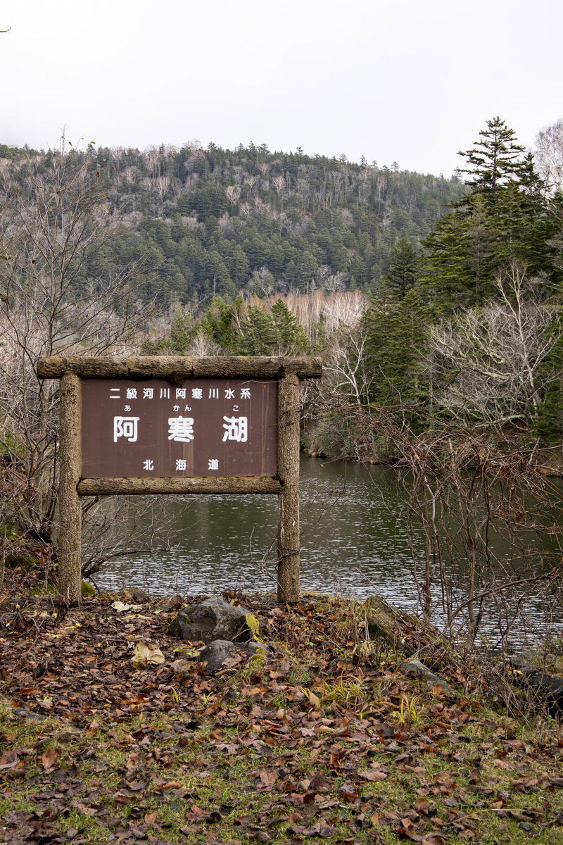 北海道・阿寒湖の湖畔に立つ木製看板と背景の湖と山々