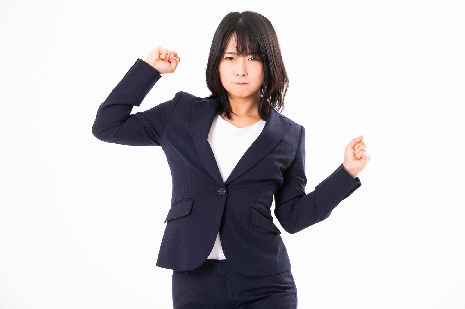 紺色スーツを着た女性が両手を握り拳で上げガッツポーズをとりながら眉をひそめて不満そうな顔をしている［モデル：にゃるる］