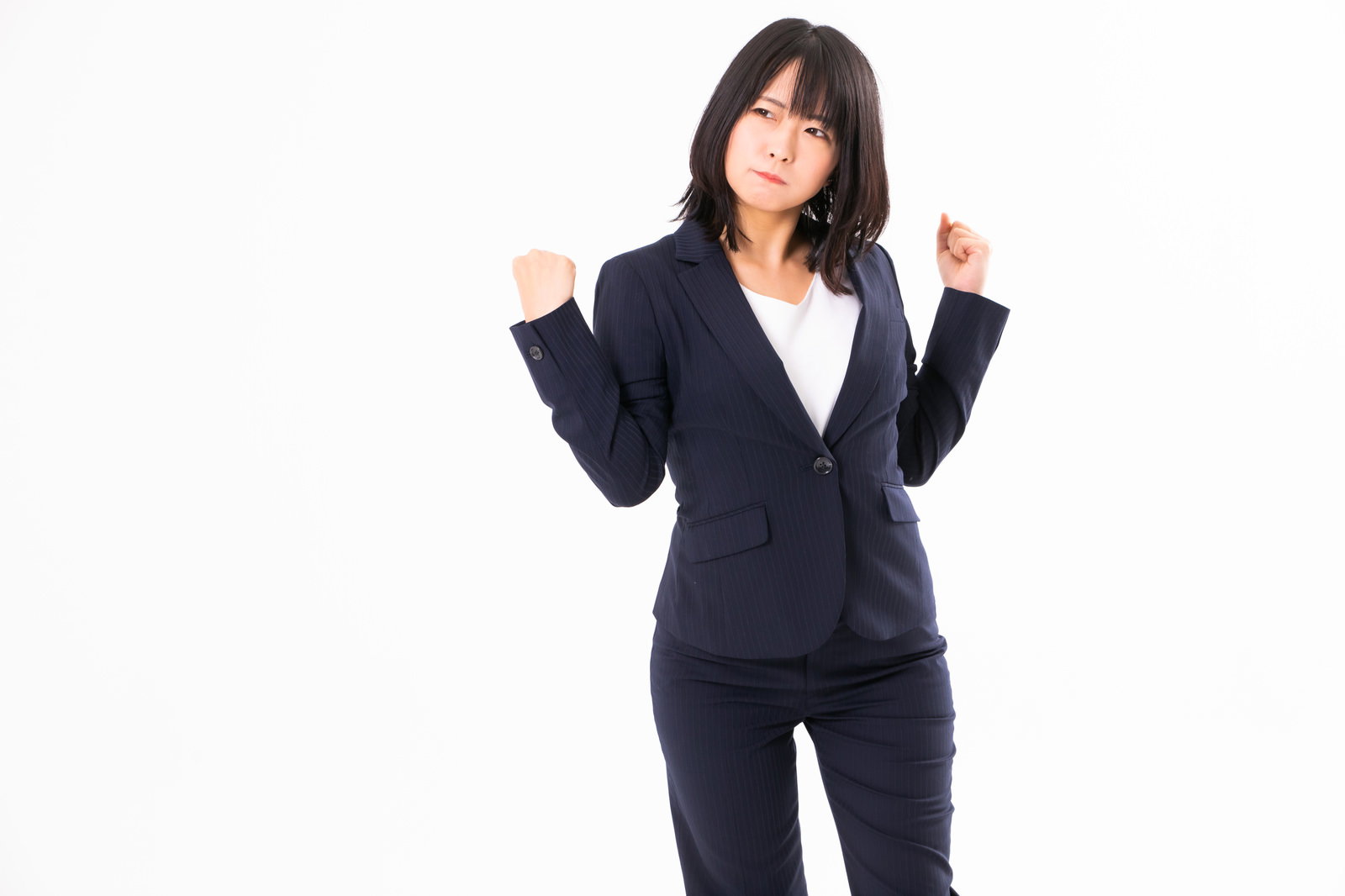 拳を握って怒りを我慢している紺色スーツの女性社員［モデル：にゃるる］