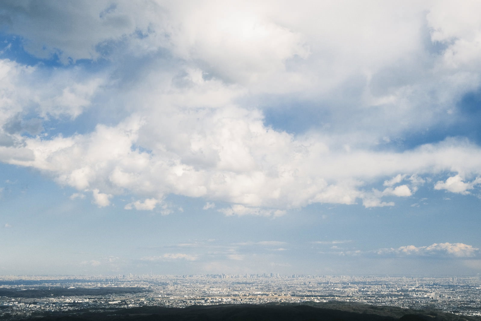 東京上空に浮かぶ巨大な白い雲と青空、下に広がる都市の風景