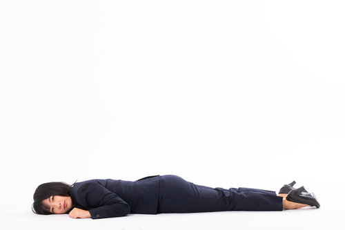 黒いスーツの会社員が床にうつ伏せで横たわる