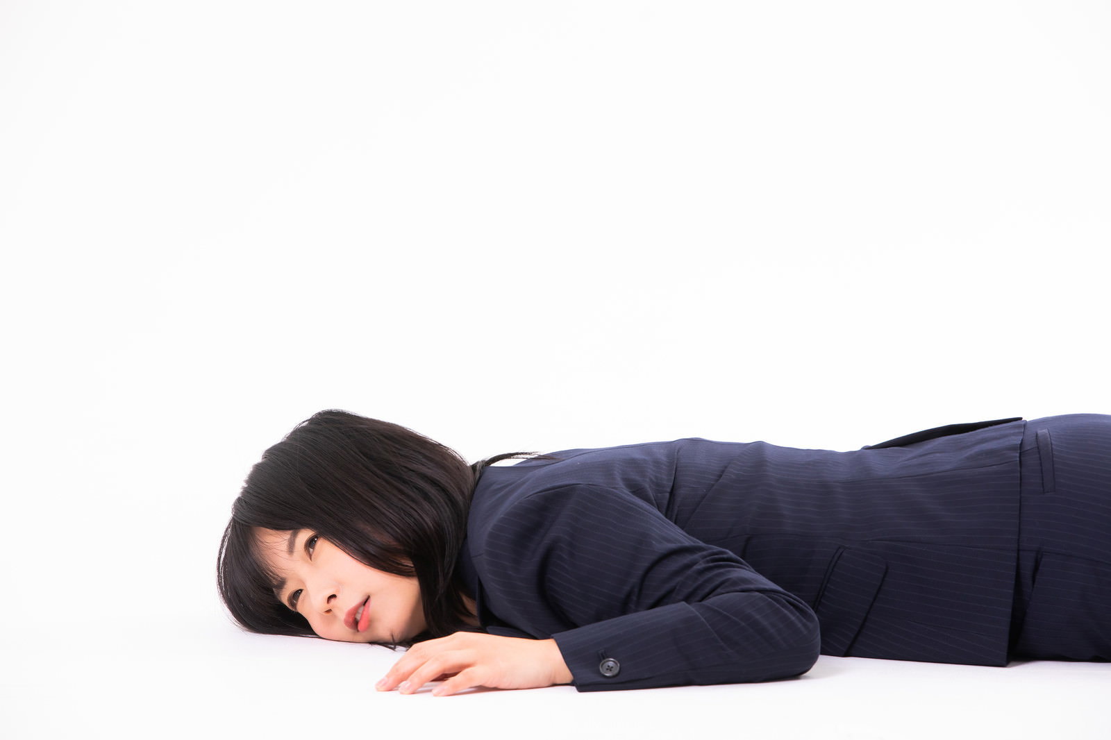 紺色のスーツを着た女性社員が床に横たわり倒れている様子［モデル：にゃるる］
