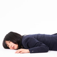 過労で床に倒れる紺色スーツの女性社員、残業による疲労とストレスの写真