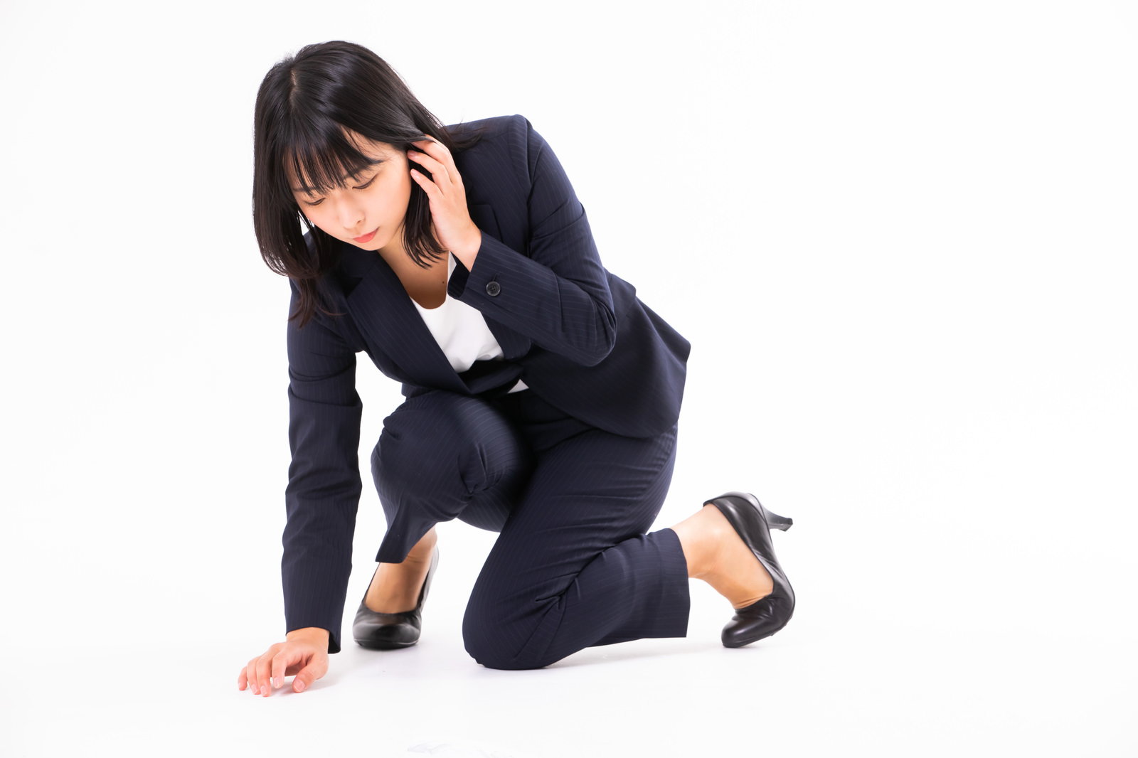 紺色のスーツを着た女性が床に膝をついてコンタクトレンズを探している［モデル：にゃるる］
