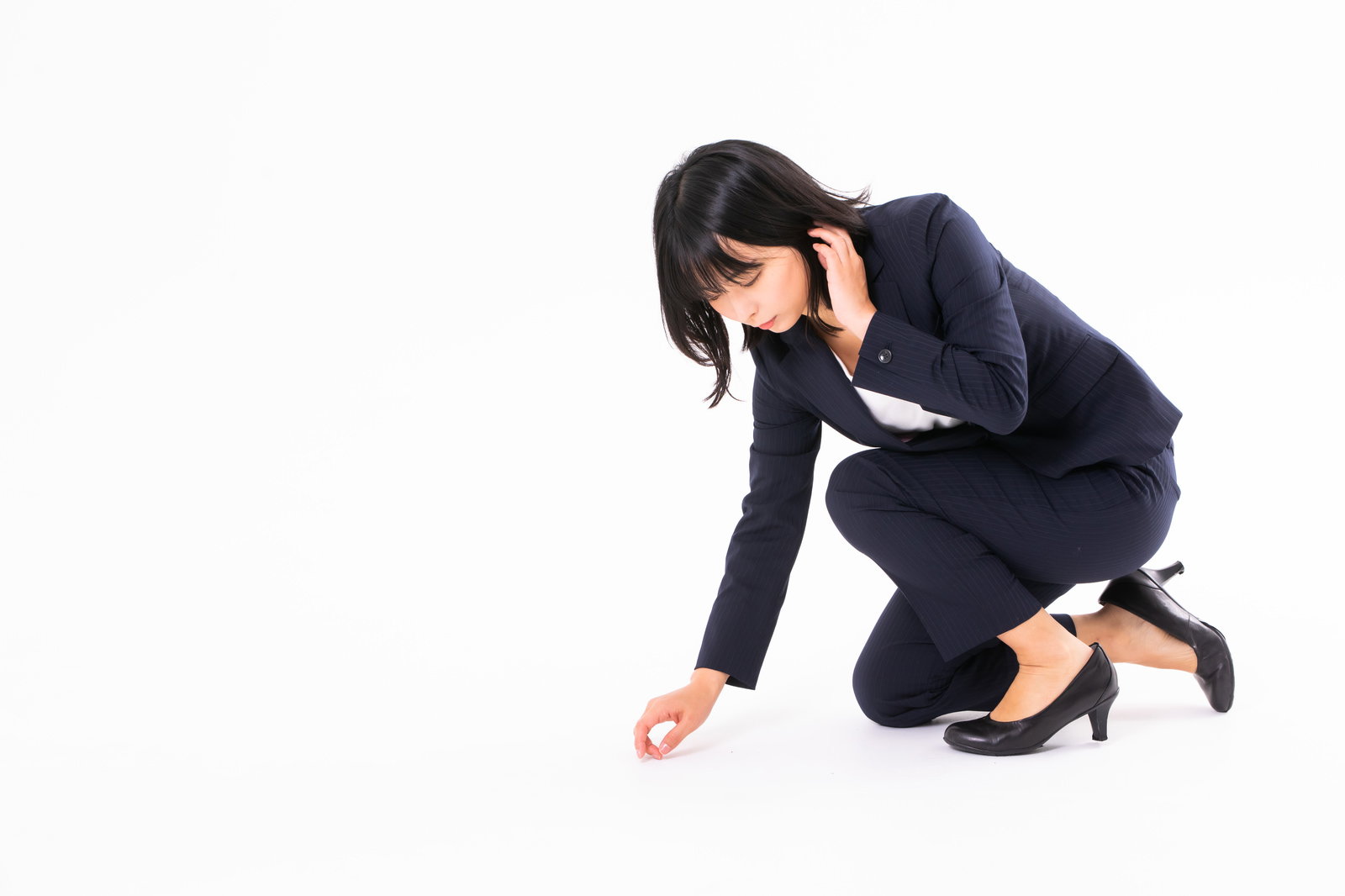 紺色のスーツを着た女性が膝をついて床の落し物を拾っている［モデル：にゃるる］