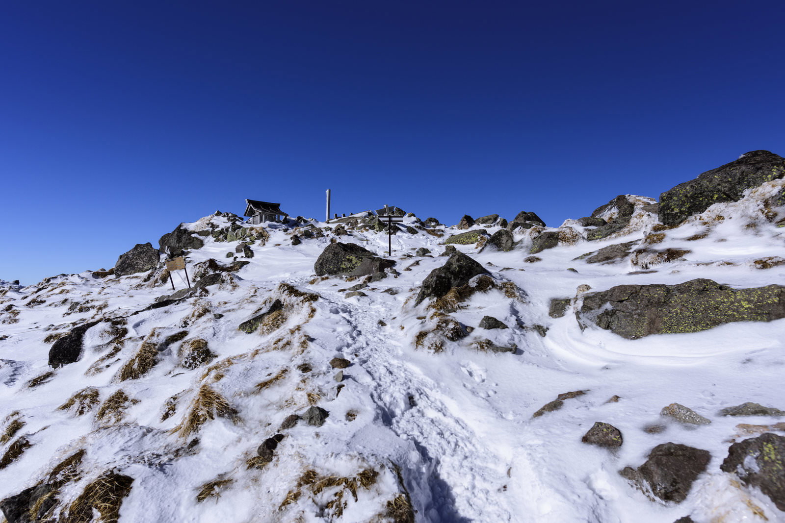 青空の下に雪が積もった日光白根山の岩だらけの山頂風景