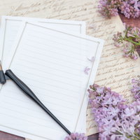 白い便箋を取り囲む淡紫色のライラックと万年筆の写真