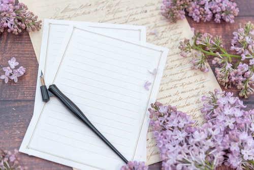 白い便箋を取り囲む淡紫色のライラックと万年筆