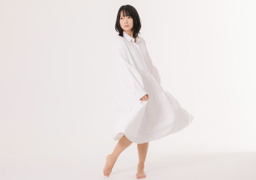 白いワンピースを着て髪をかき上げる爽やかなポーズの女性