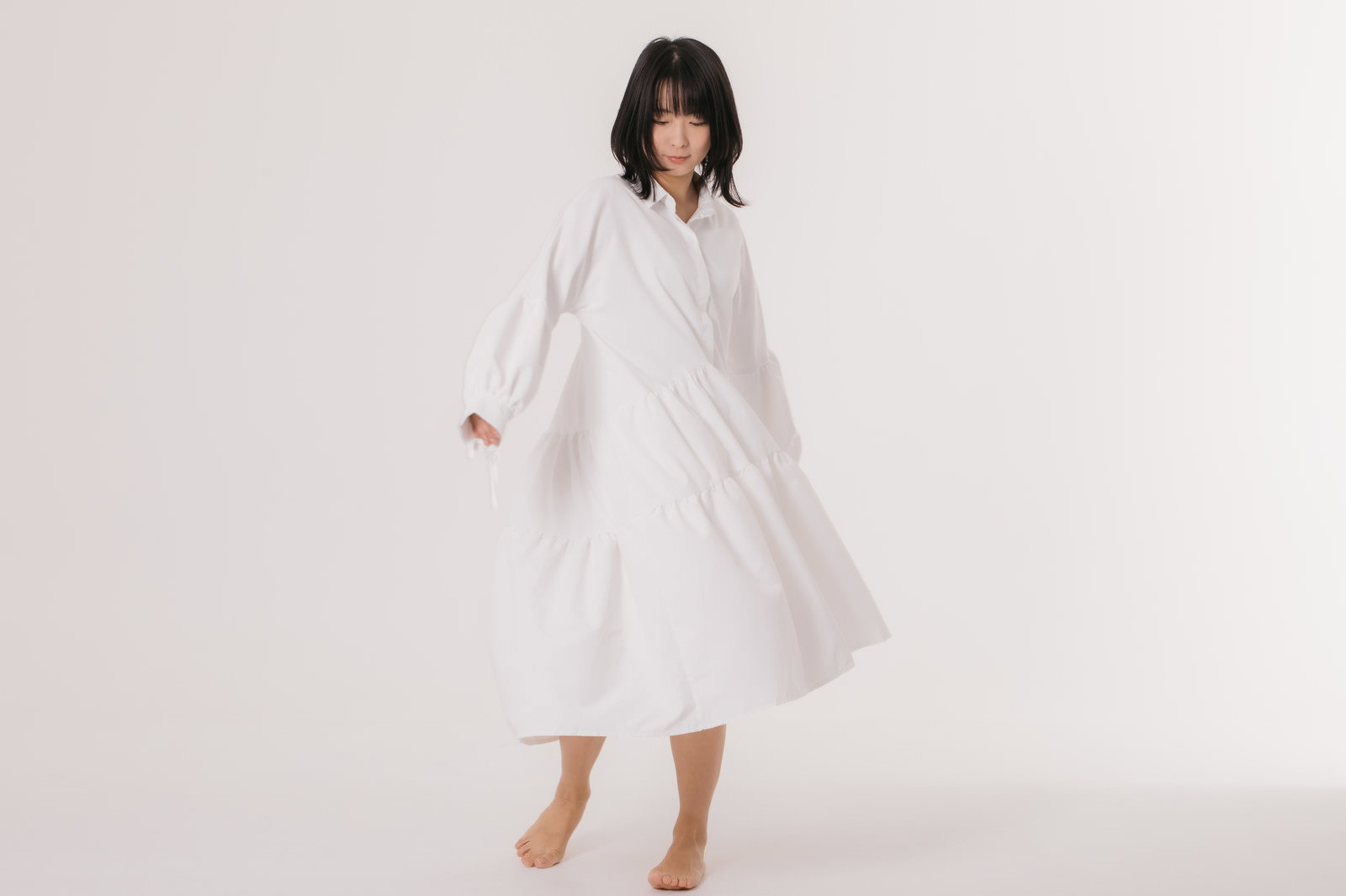 白いワンピースの裾を手で持ち上げてポーズを取る女性［モデル：にゃるる］