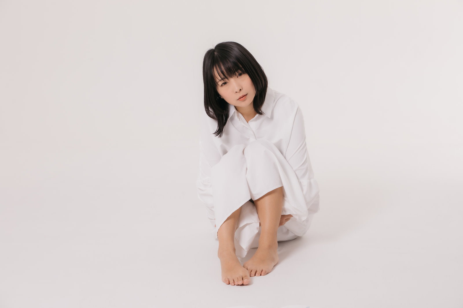 白いシャツを着て膝を抱えて座る女性のリラックスした様子［モデル：にゃるる］