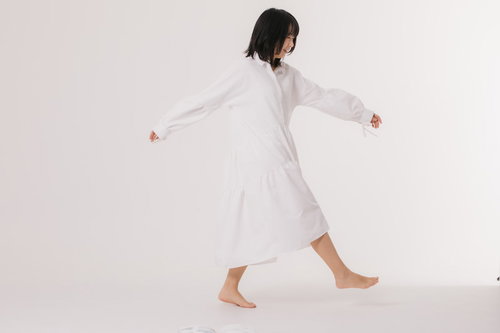 白いワンピース姿で両腕を広げて歩き出す女性の後ろ姿