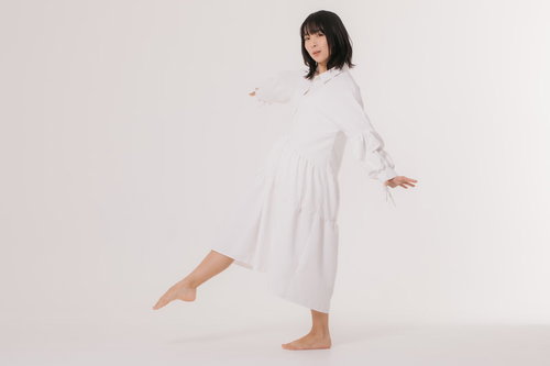 白いワンピースで片足を上げてバランスをとる女性モデル