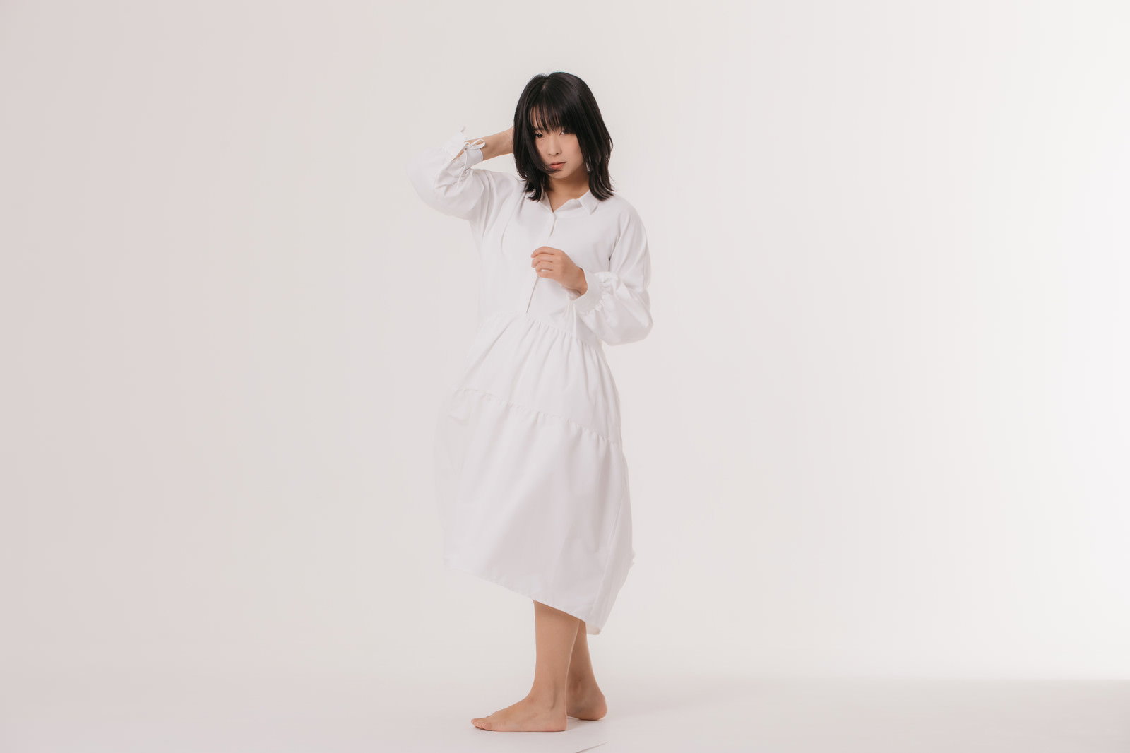 白いワンピースを着て髪を押さえながら振り返る女性モデル［モデル：にゃるる］