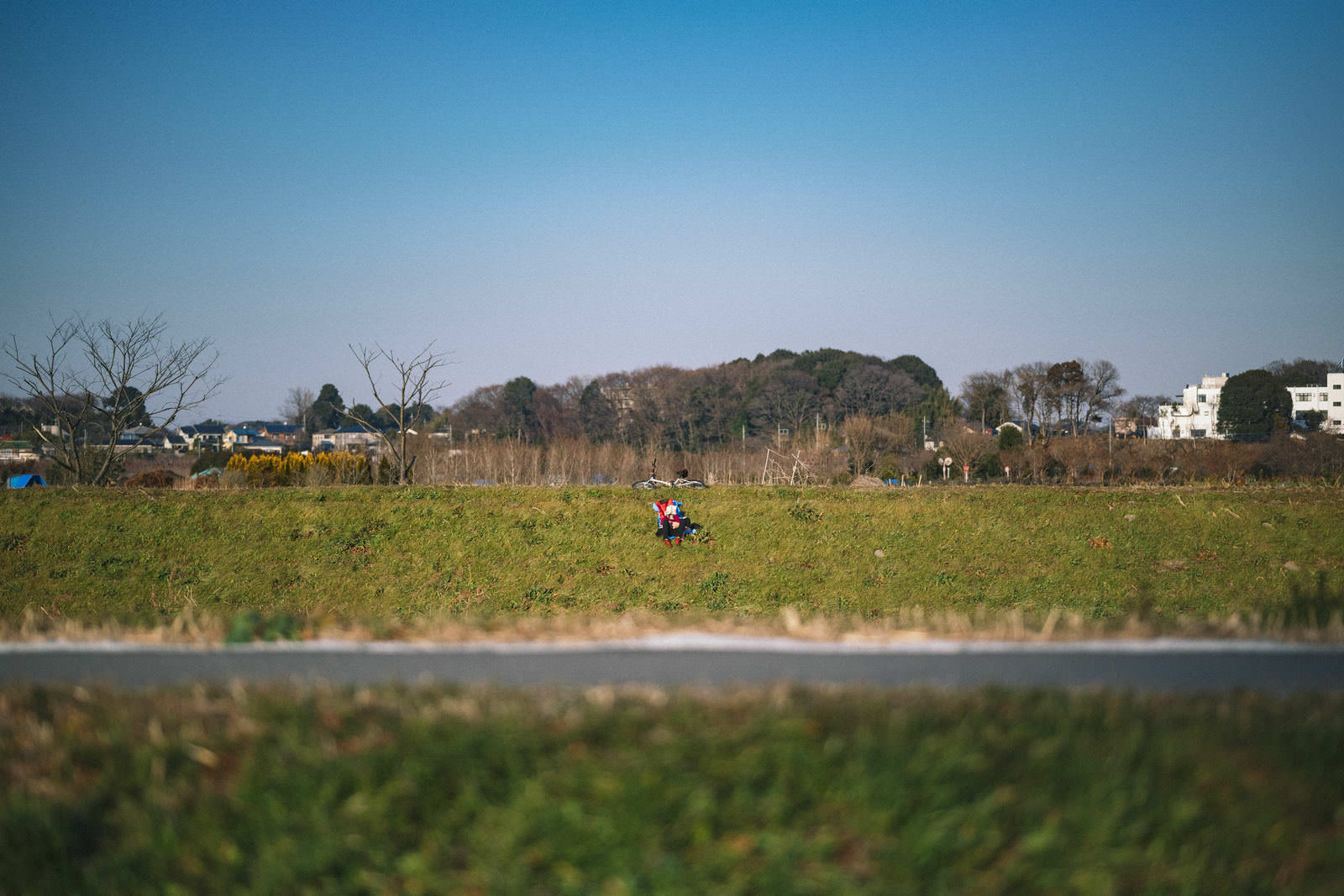 河川敷の土手で自転車の横に座って休憩するチャリダー