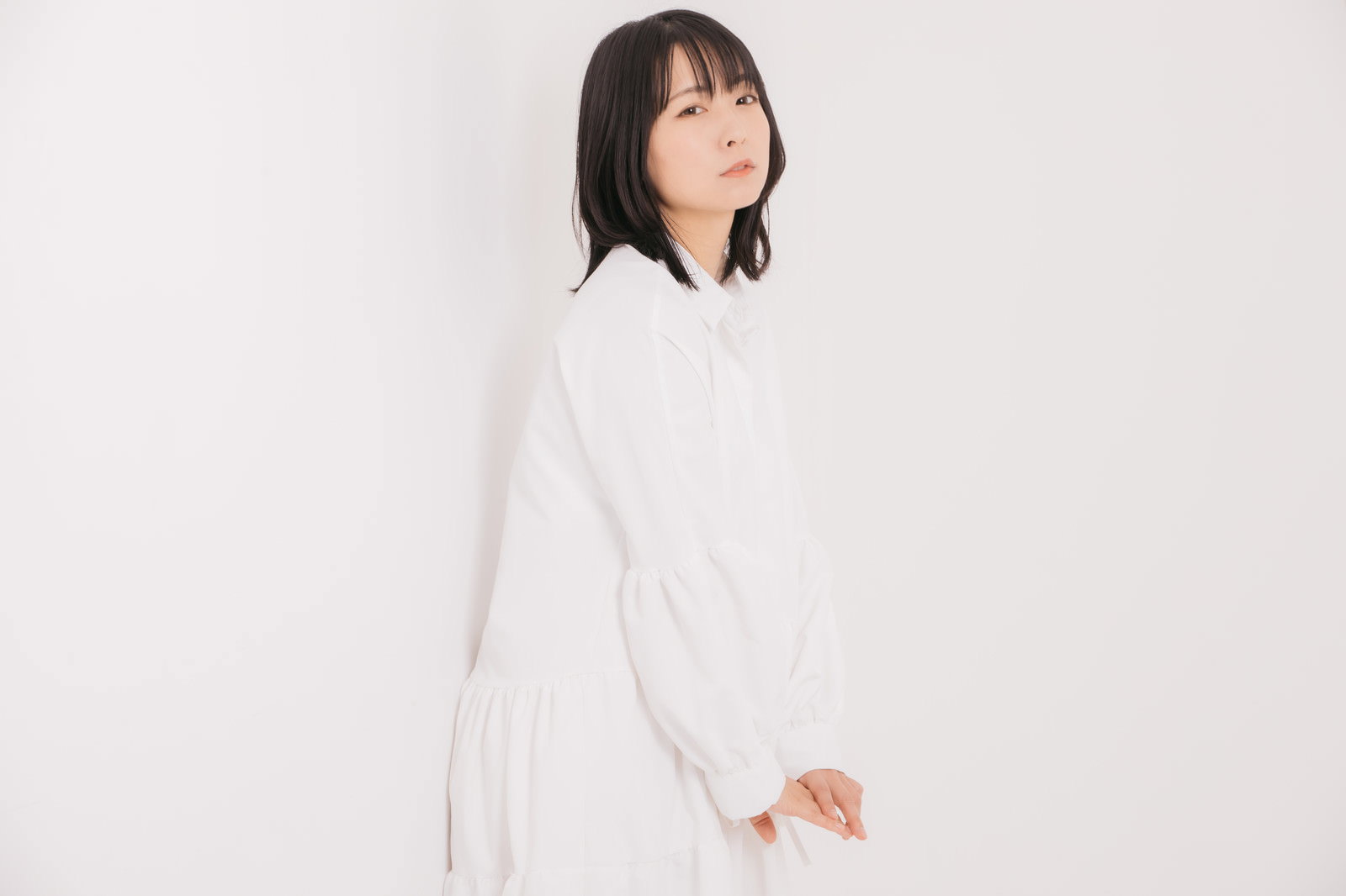 白い服を着た女性が壁に背を向けて振り返るポーズをしている［モデル：にゃるる］