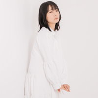 白い衣装で壁に背を向けてポージングする女性の写真
