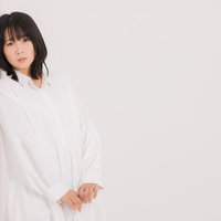 白い服を着て壁にもたれるポーズを取る女性の写真