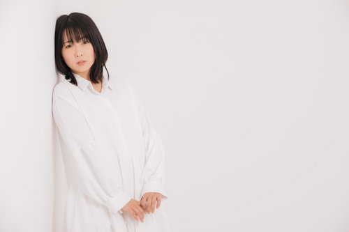 白い服を着て壁にもたれるポーズを取る女性