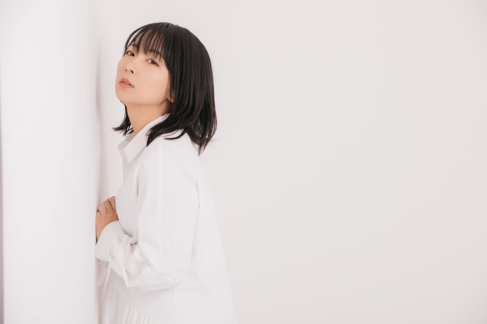 白い服を着た女性が壁に寄りかかり横顔を向いている様子［モデル：にゃるる］
