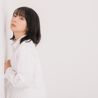 白い服を着た女性が壁に寄りかかるポージングの写真