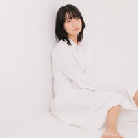 白いトップスを着て壁際に座り込む女性モデルの写真