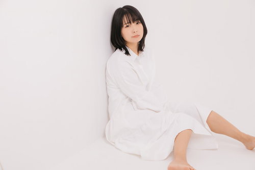 白いトップスを着て壁際に座り込む女性モデル