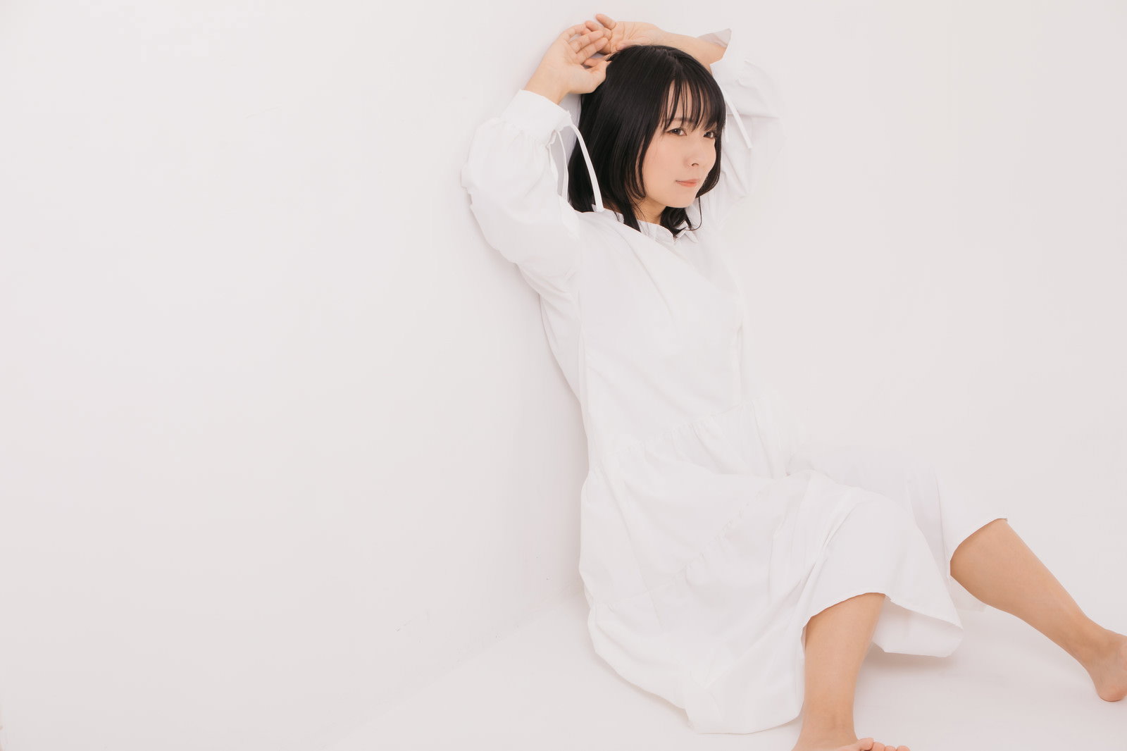 白い長袖を着た女性が壁に寄り掛かって座り込みポージングしている［モデル：にゃるる］