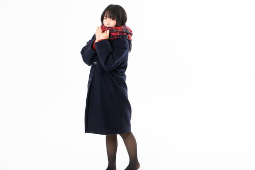 赤いマフラーを口元まで巻いて身を縩めるコート姿の女性