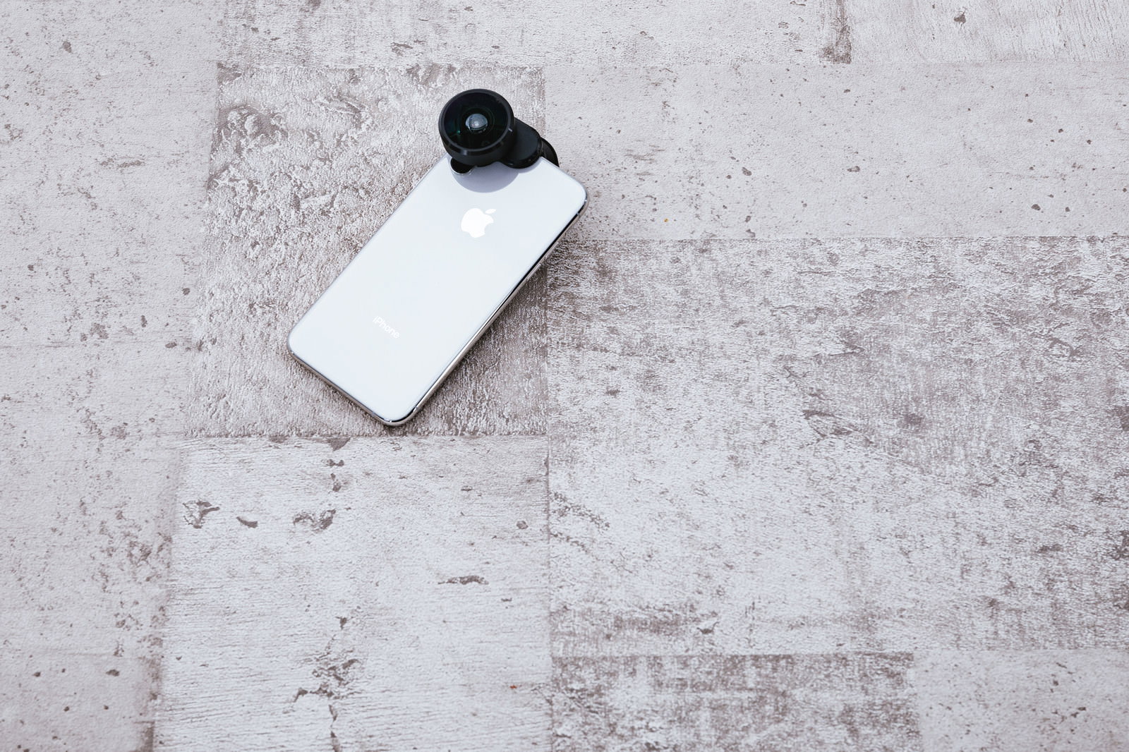 コンクリートの床に置いた外付けレンズ付きのiPhone