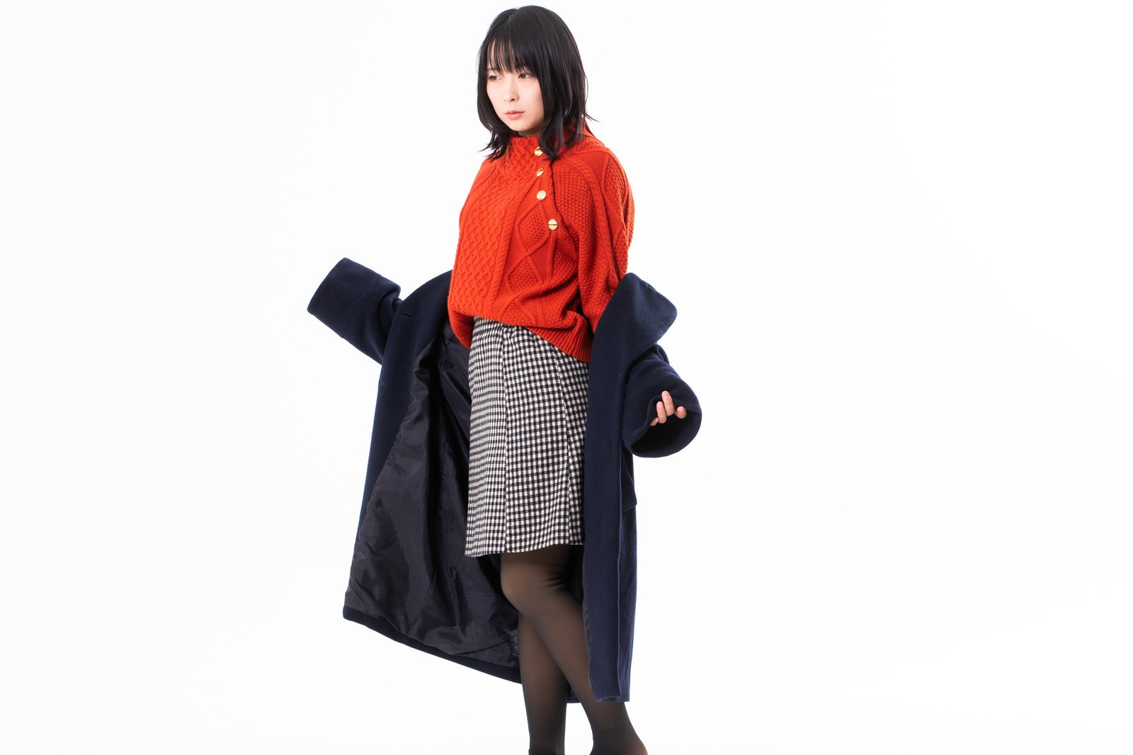 黒いコートを脱ぎかける赤いトップスとグレーのスカートを着た女性［モデル：にゃるる］
