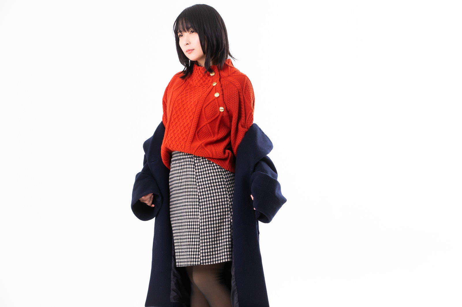 室内で紺色のコートを脱いで手に持つ、赤いセーターを着た女性［モデル：にゃるる］